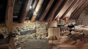 A cozy attic room with a stone wall, wooden beams, a rustic table, and comfortable seating. - Le buron de Perrier  (Saint urcize)