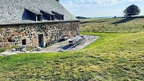 A stone building with a sloped roof, a small porch, and a view of a grassy field. - Le buron de Perrier  (Saint urcize)