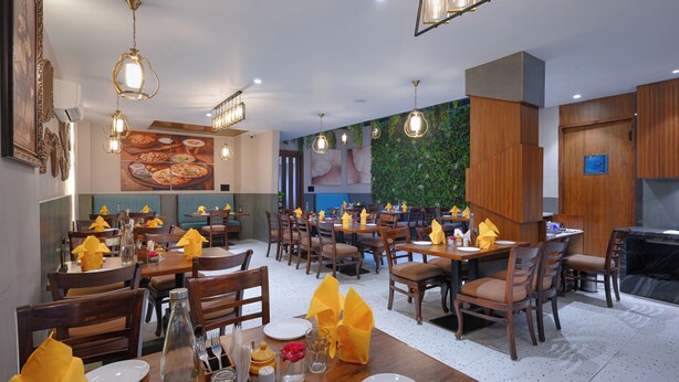 Un restaurant amb taules i cadires de fusta, gots de paper grocs i una paret verda decorada amb plantes.