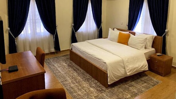 Une chambre d’hôtel avec un grand lit, un bureau et une chaise. Un climatiseur est fixé au mur.