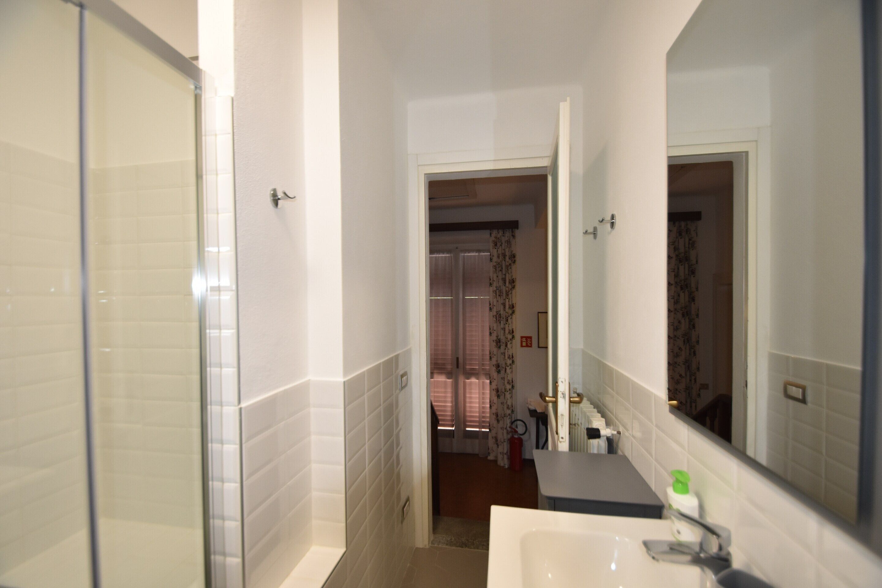 Un bagno con cabina doccia in vetro, un lavabo con specchio e una porta che dà su un'altra stanza.