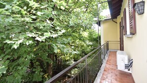 A balcony with a metal railing, a brick floor, and a yellow wall with a window and a wall-mounted light fixture. - Holiday Home in Meina (Meina)