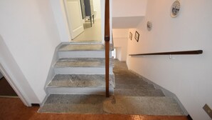 A staircase with stone steps and a wooden handrail, leading to a room with a white door and a view of a bathroom. - Holiday Home in Meina (Meina)