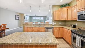 A modern kitchen with granite countertops, wooden cabinets, stainless steel appliances, and pendant lighting.