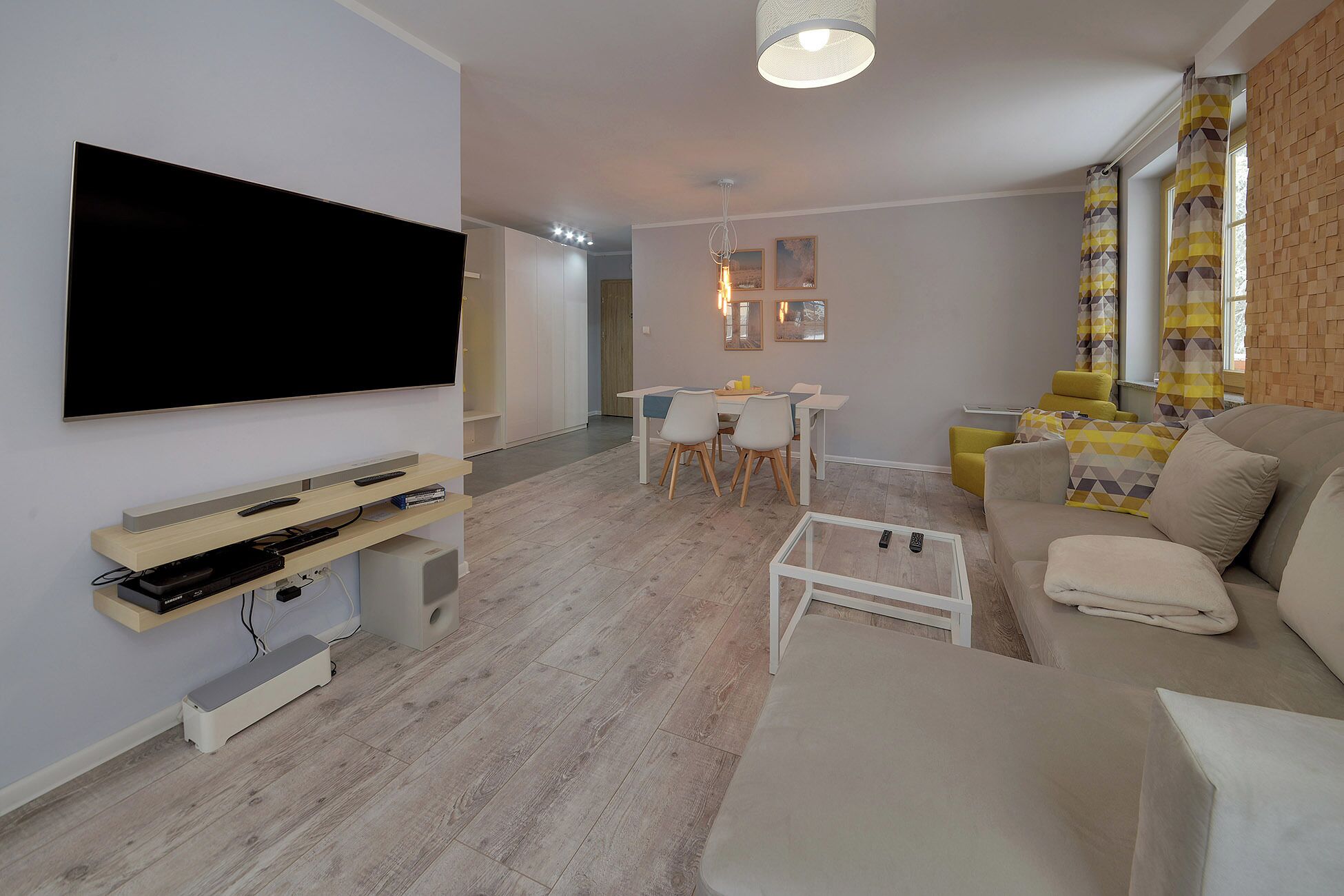 A modern living room with a flat-screen TV, a sofa, a coffee table, and a dining area with chairs and a table.