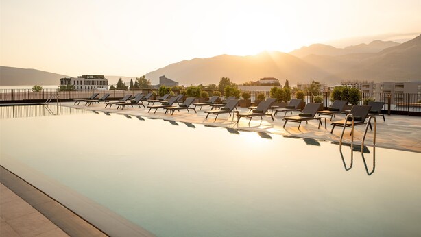 A swimming pool with lounge chairs and a view of mountains and a building in the background. - SIRO Porto Montenegro (Tivat)