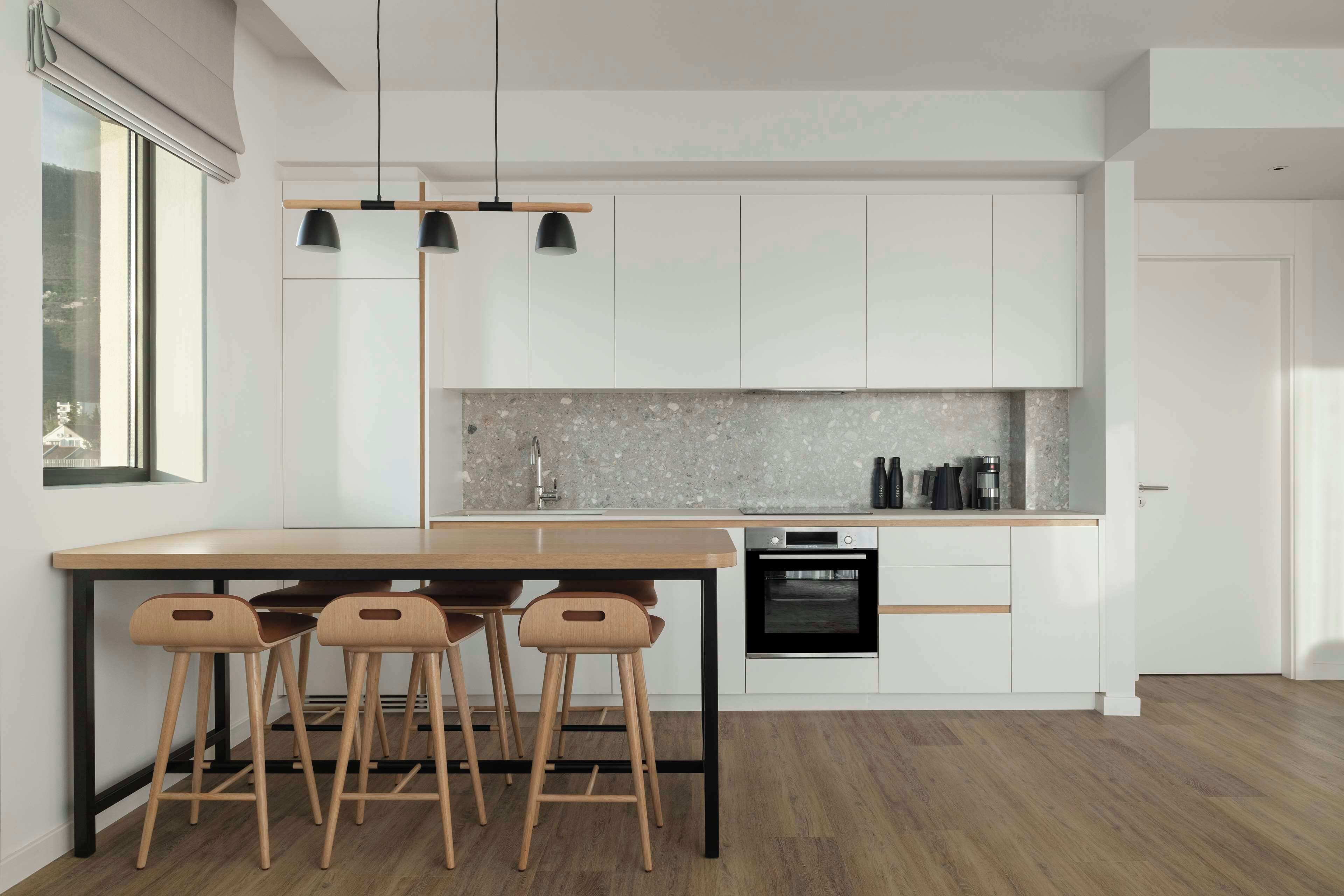 Una cocina moderna con una isla de madera, taburetes de bar, horno empotrado e iluminación colgante.