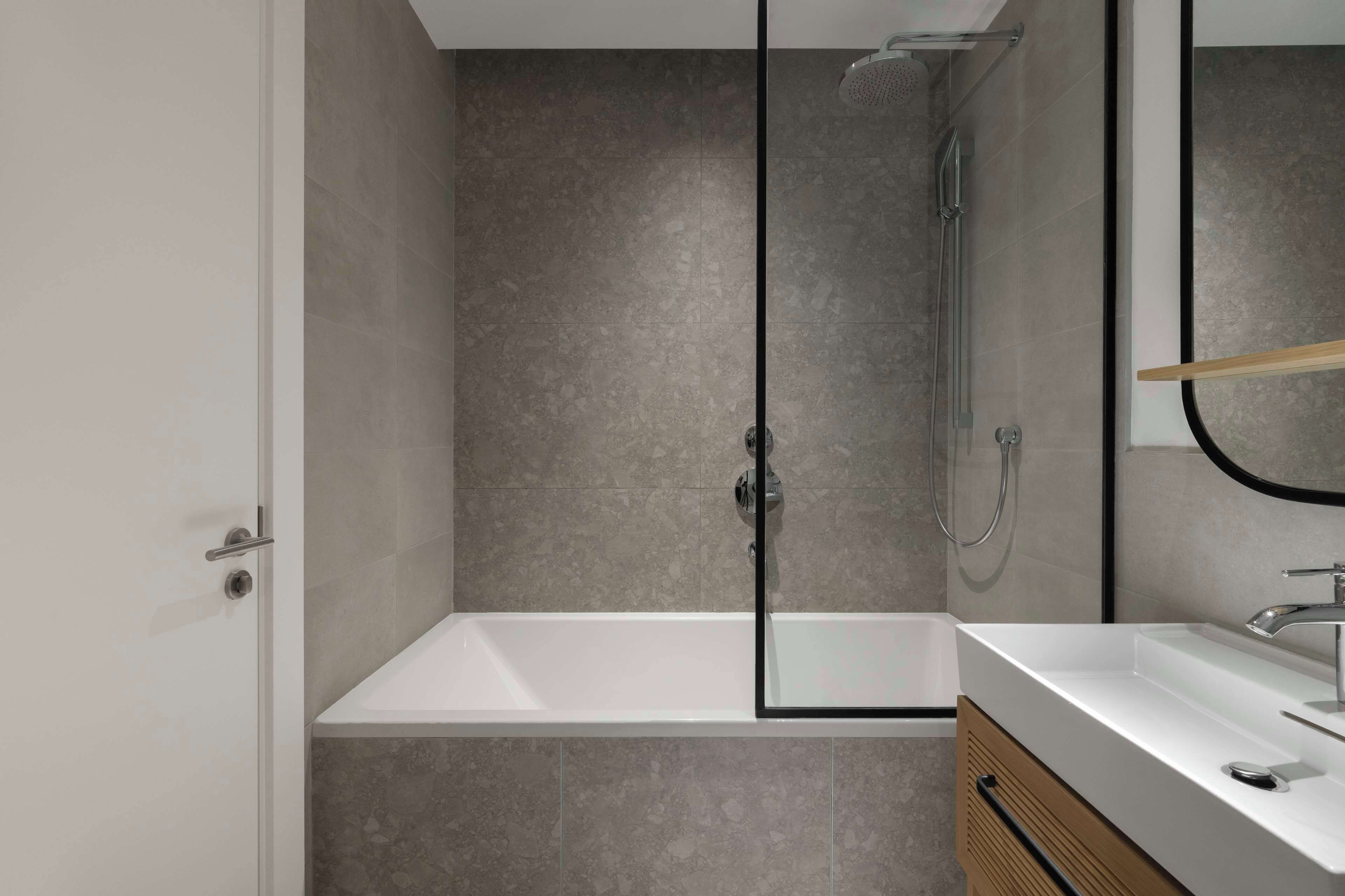 Un baño moderno con ducha envuelta en vidrio, bañera blanca y tocador de madera con espejo.