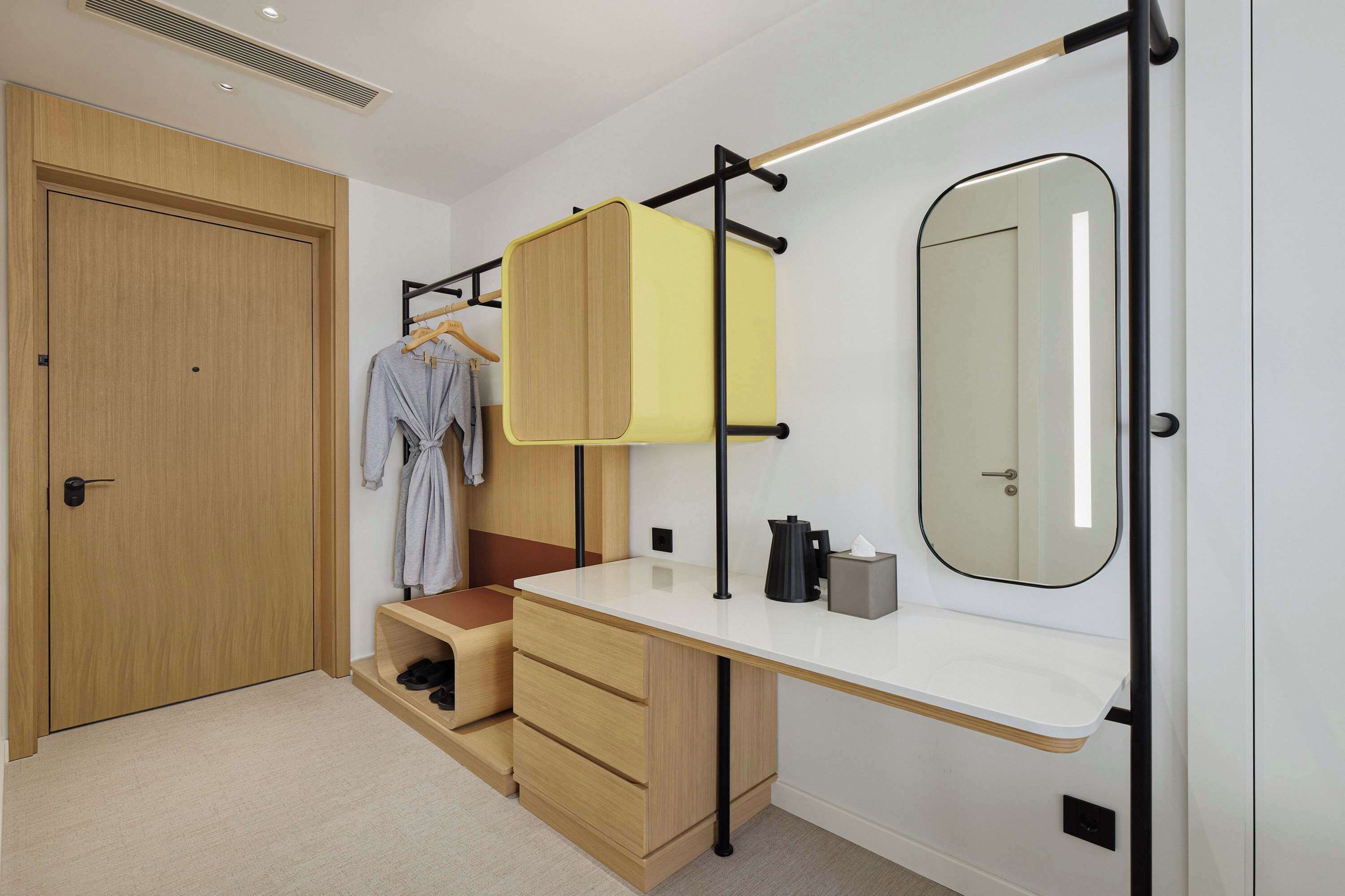 Un dormitorio moderno con un armario de madera, un escritorio empotrado con espejo y un perchero.