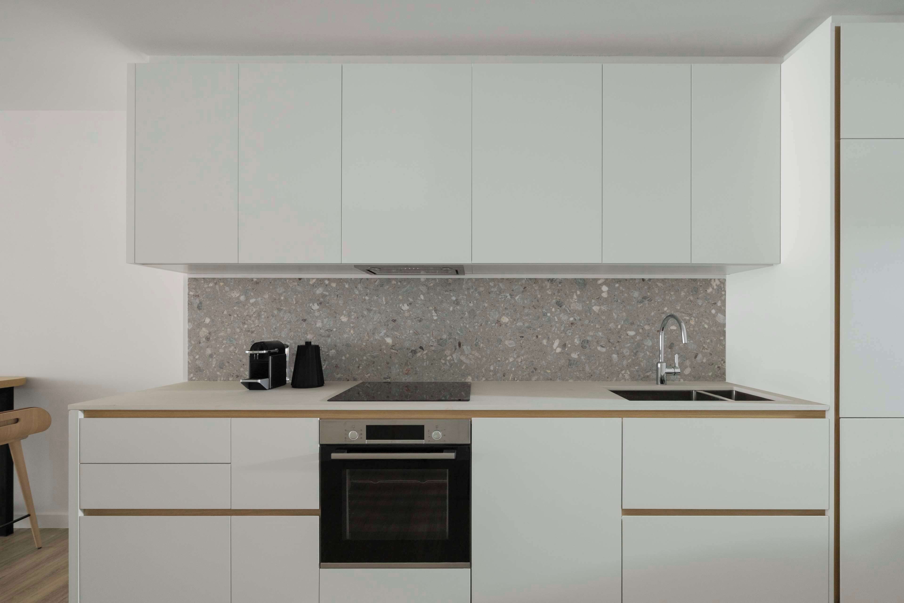 A modern kitchen with white cabinets, a granite countertop, a built-in oven, and a sink.