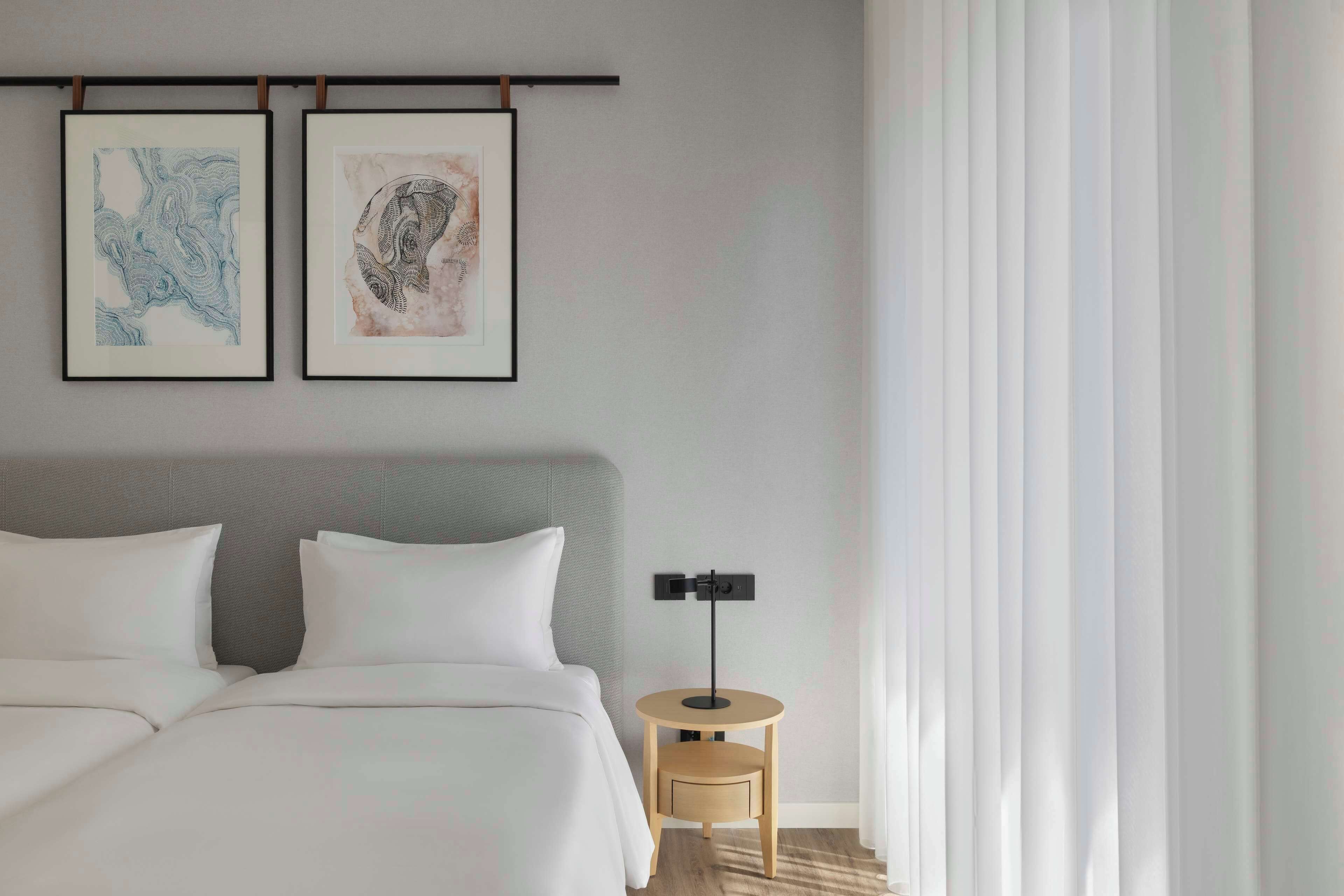 Ein Hotelzimmer mit einem Bett, zwei gerahmten Kunstwerken, einem Nachttisch und einer Lampe.