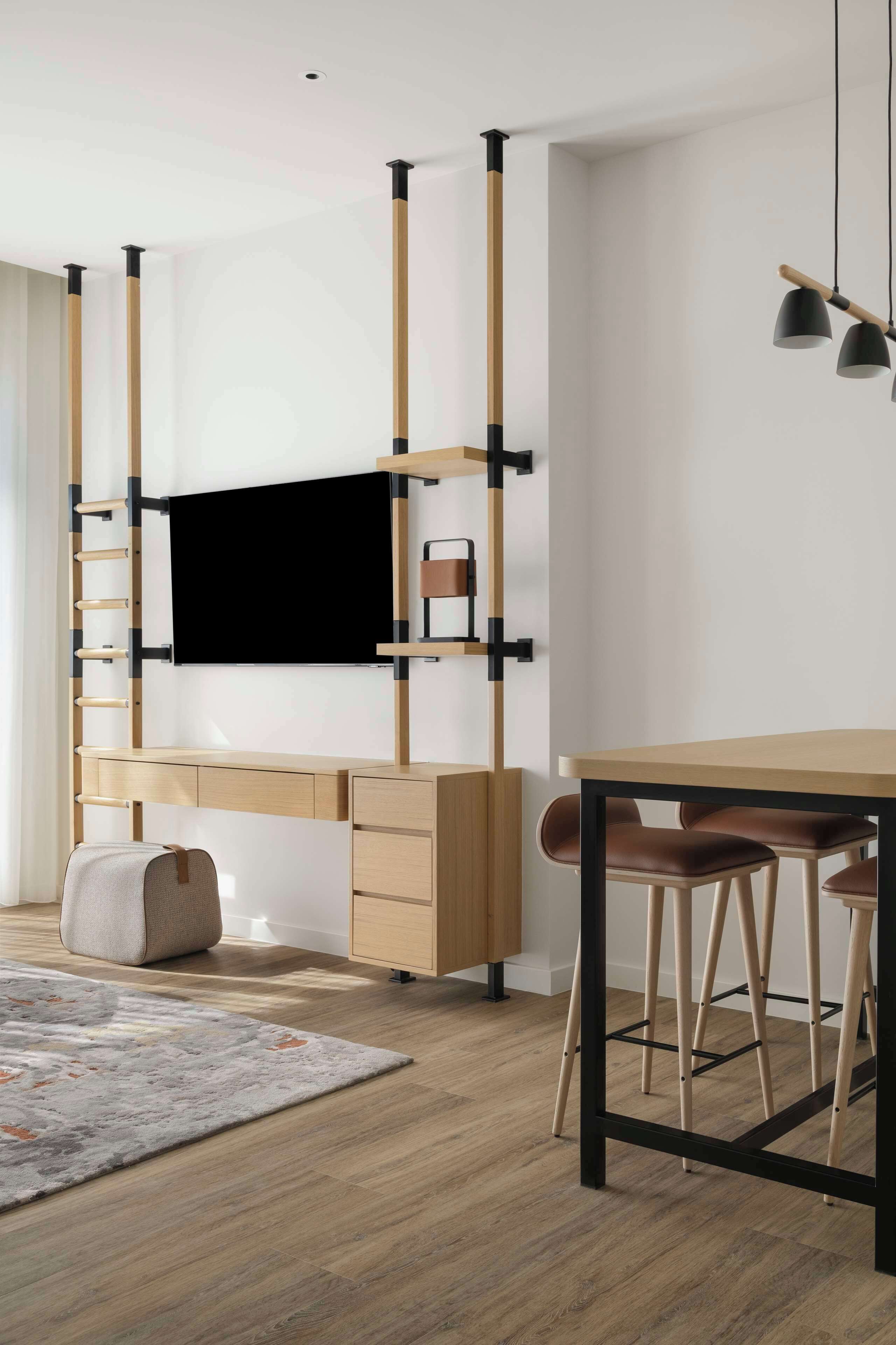 A modern room with a wooden desk, a TV mounted on a wall, a sofa, and a dining table with chairs.