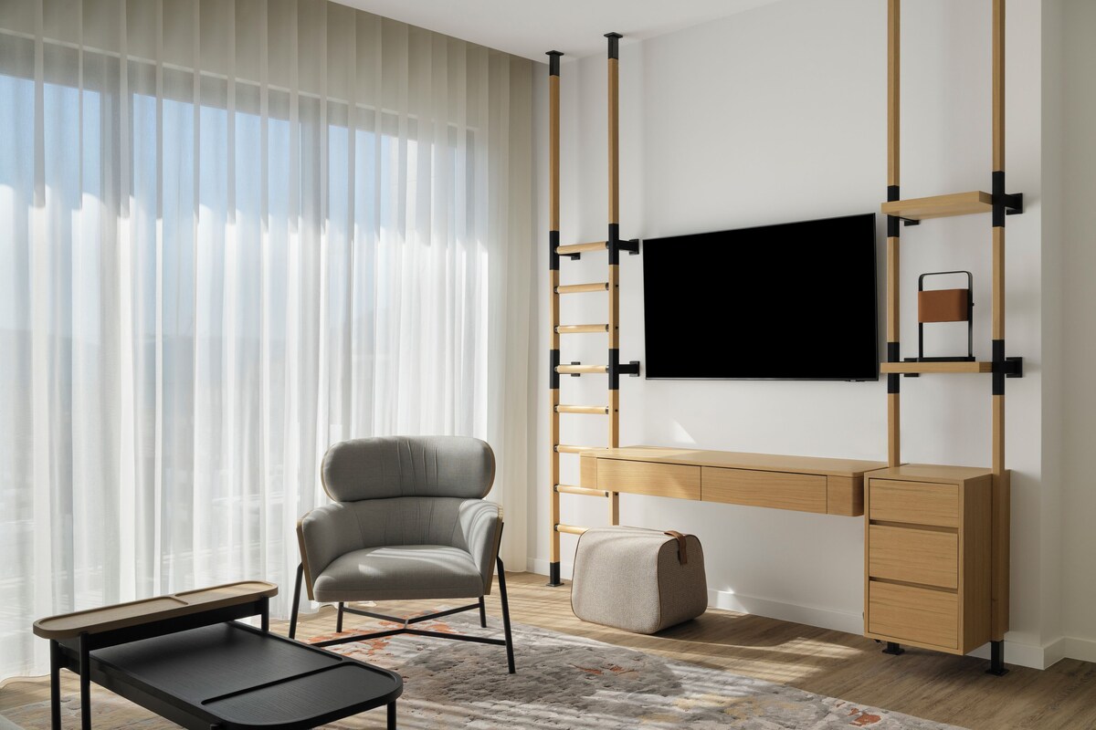 A modern room with a desk, chair, TV, and a window with blinds.