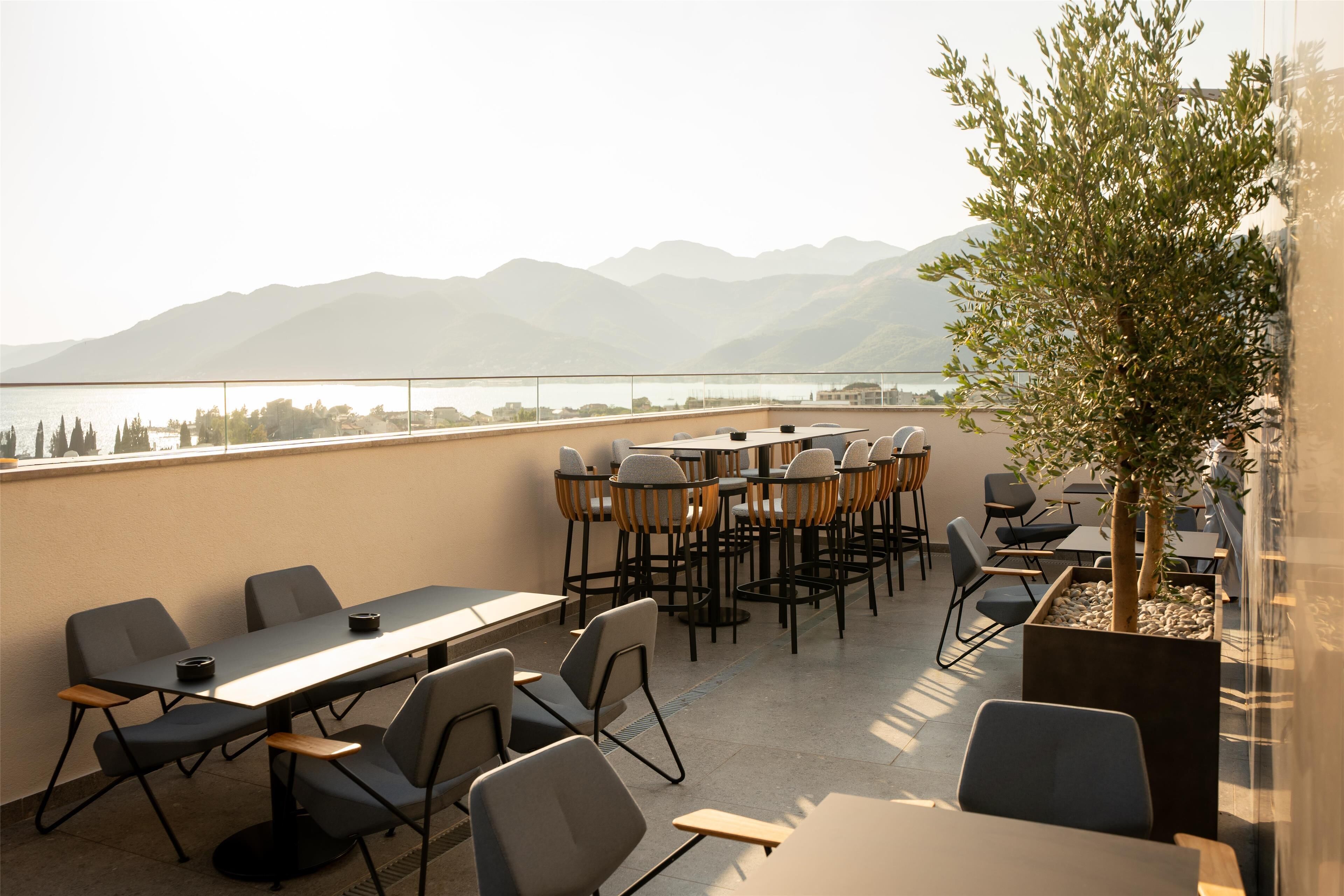 A terrace with tables and chairs, a view of mountains, and a tree.