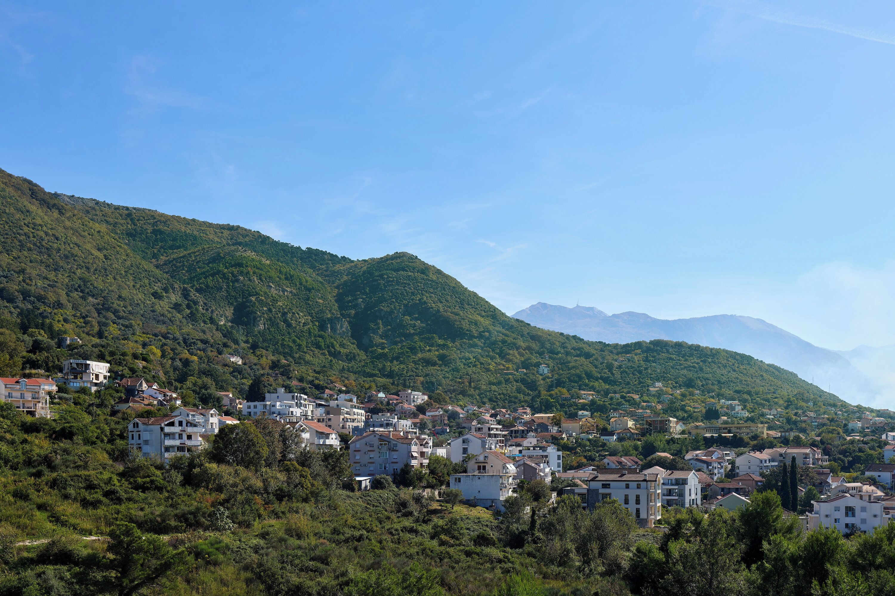 Une ville construite sur une colline, avec des bâtiments nichés au milieu de collines verdoyantes et de montagnes qui se dressent à l’arrière-plan.