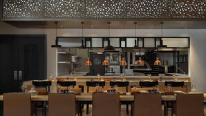 A modern dining area with a central kitchen, pendant lighting, and a ceiling with a polka dot pattern. - SIRO Porto Montenegro (Tivat)