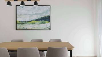 A modern dining area with a wooden table and grey upholstered chairs, a framed abstract painting above, and pendant lighting.