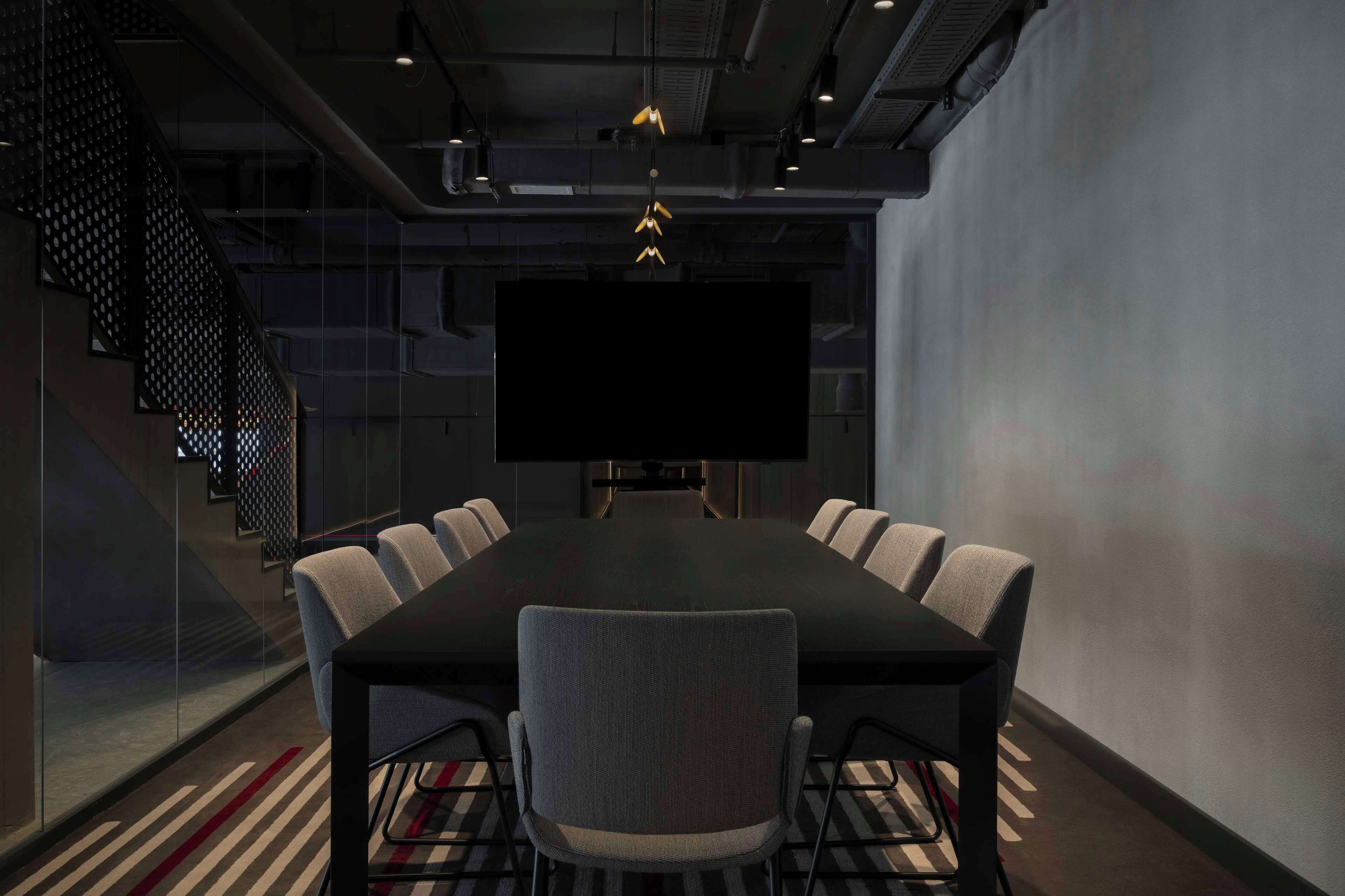 A conference room with a large table, six chairs, a TV screen, and a staircase.