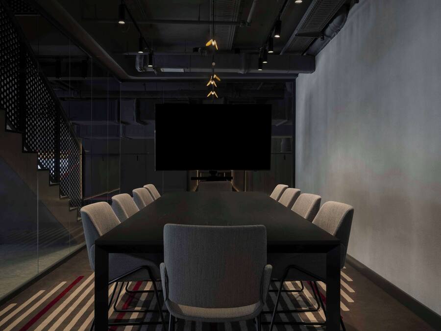 A conference room with a large table, six chairs, a TV screen, and a staircase.