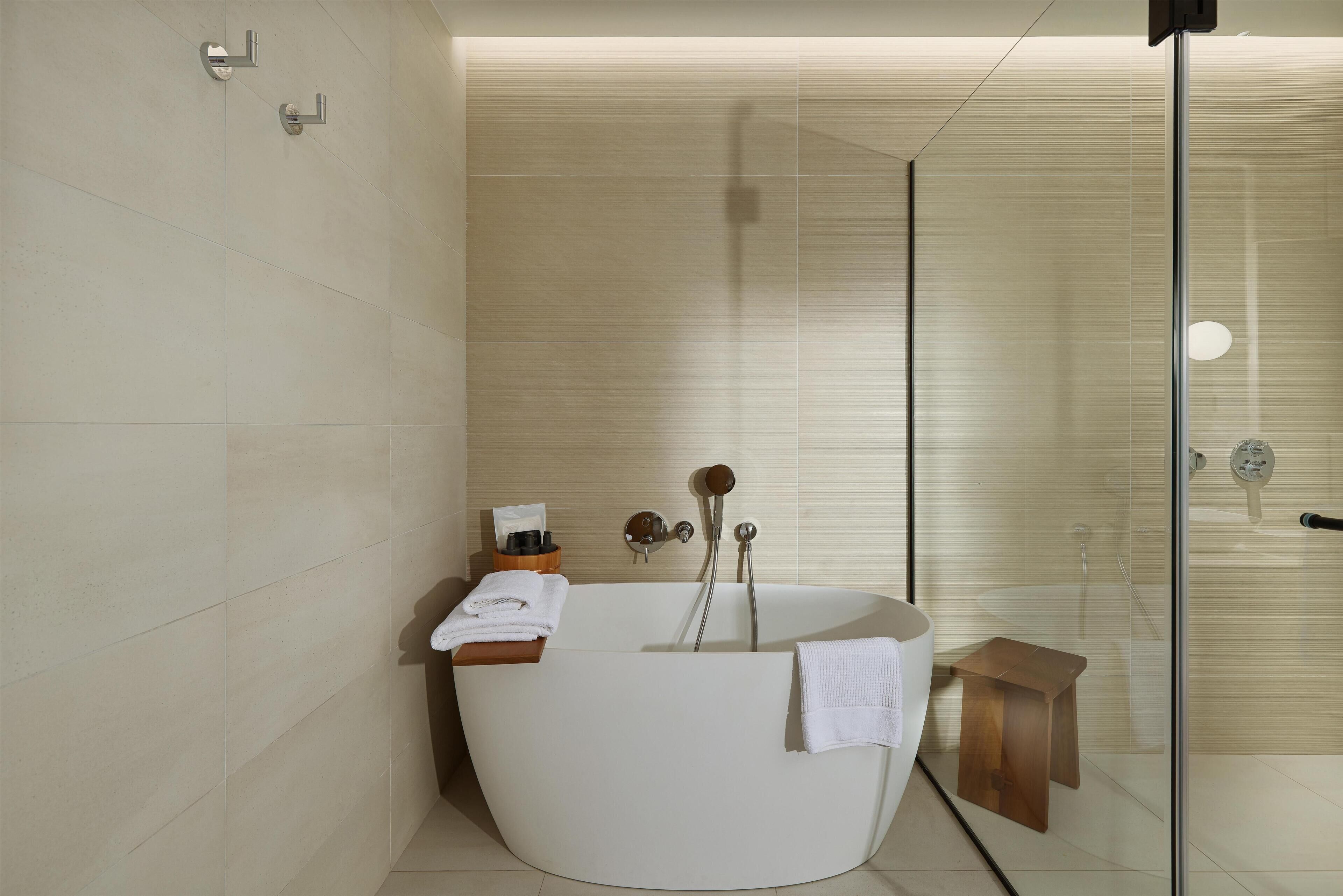 Un bagno moderno con una vasca freestanding, uno spazio doccia in vetro e un piccolo sgabello di legno.