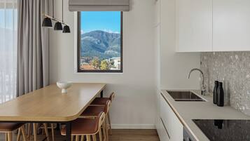 Een moderne keuken met een houten eettafel, stoelen, een ingebouwde gootsteen en een raam met uitzicht op bergen.