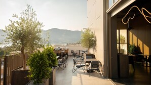 An outdoor seating area with tables and chairs, a view of mountains, and a building with large windows. - SIRO Porto Montenegro (Tivat)