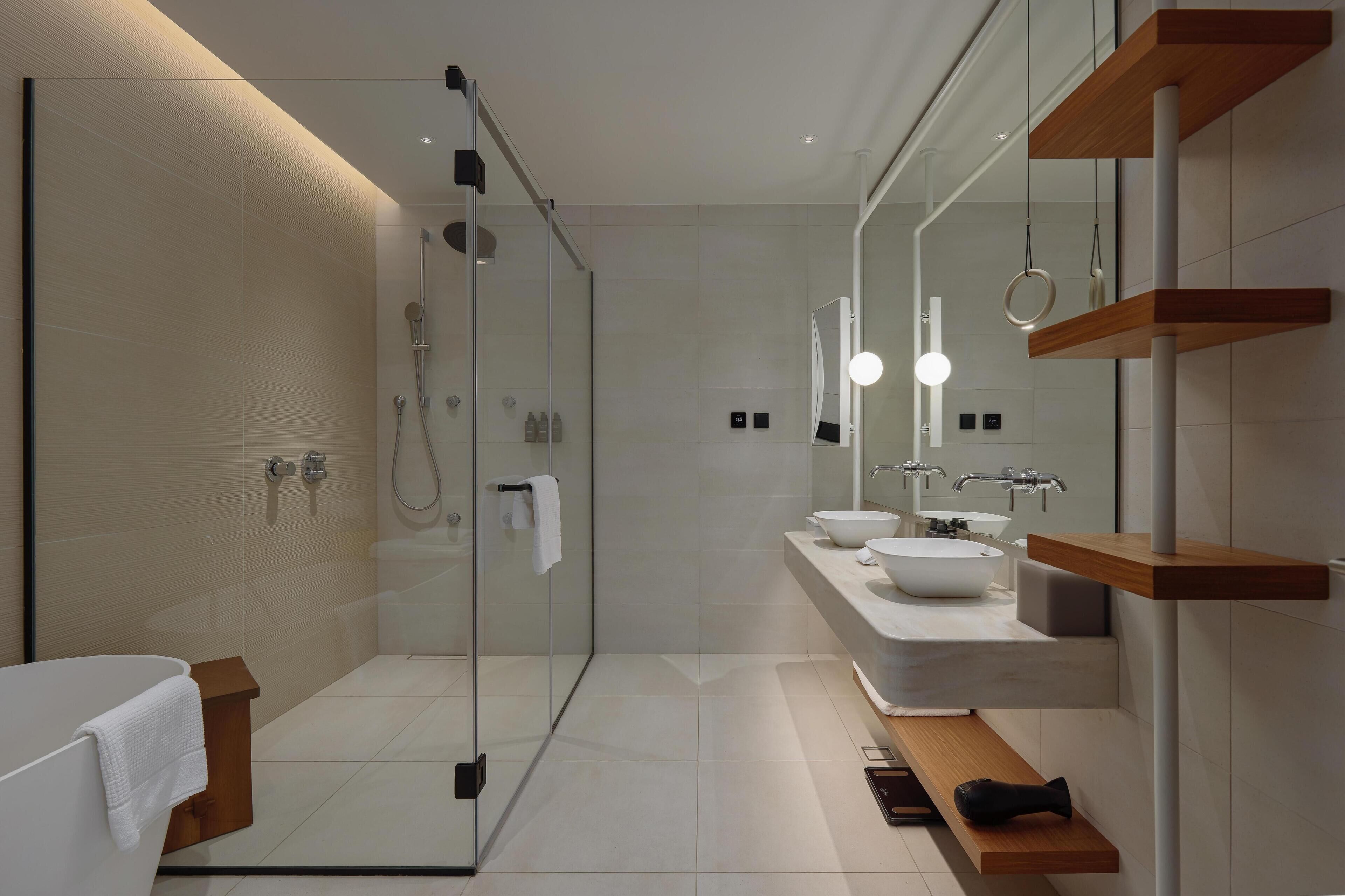 A modern bathroom with a glass-enclosed shower, a white bathtub, and a vanity with two sinks.