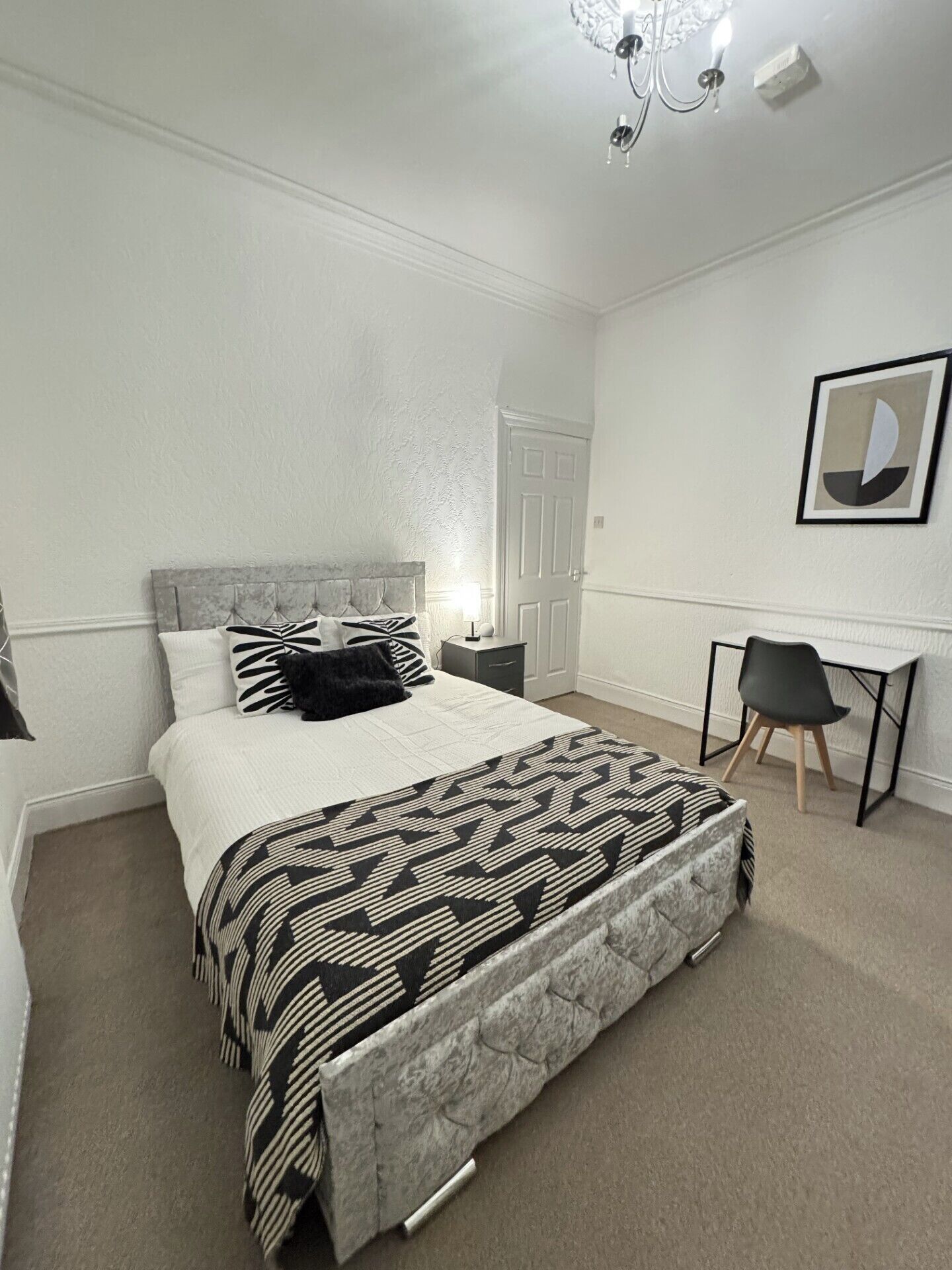 A bedroom with a bed, bedside table, chair, desk, and a framed picture on the wall.