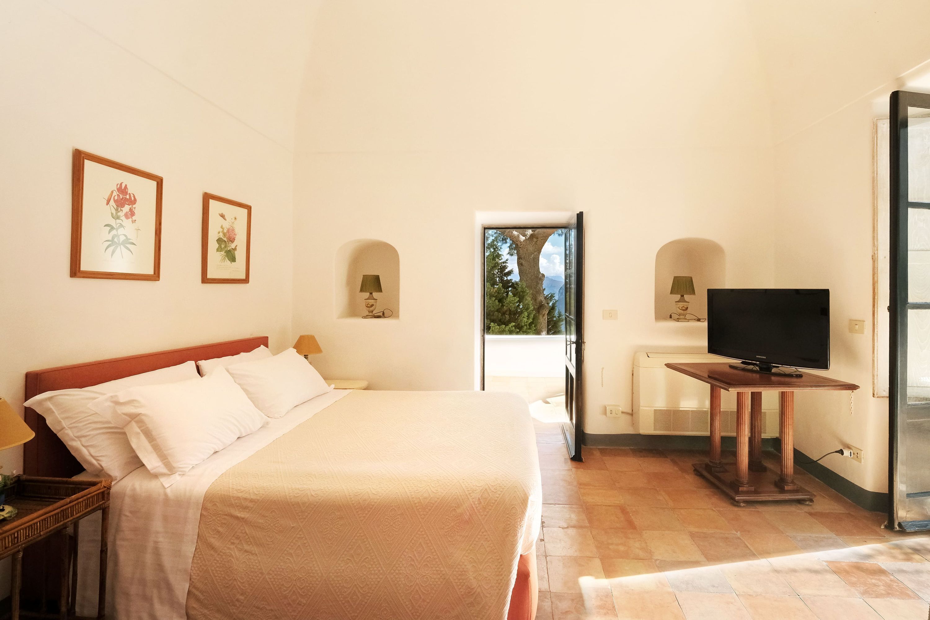 Ein Hotelzimmer mit einem großen Bett, einem Fernseher auf einem Holztisch und zwei gerahmten Blumenbildern an der Wand.