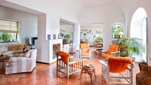 A spacious living area with a sofa, chairs, and a fireplace. There are plants and a television in the room. - Villa Amelia in Capri (Capri)