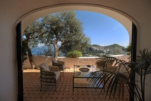 A patio with a glass table, chairs, and a view of a tree and landscape.