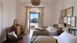 A bedroom with two beds, a wooden dresser, a chair, a hanging light fixture, and framed pictures on the wall. - Villa Amelia in Capri (Capri)