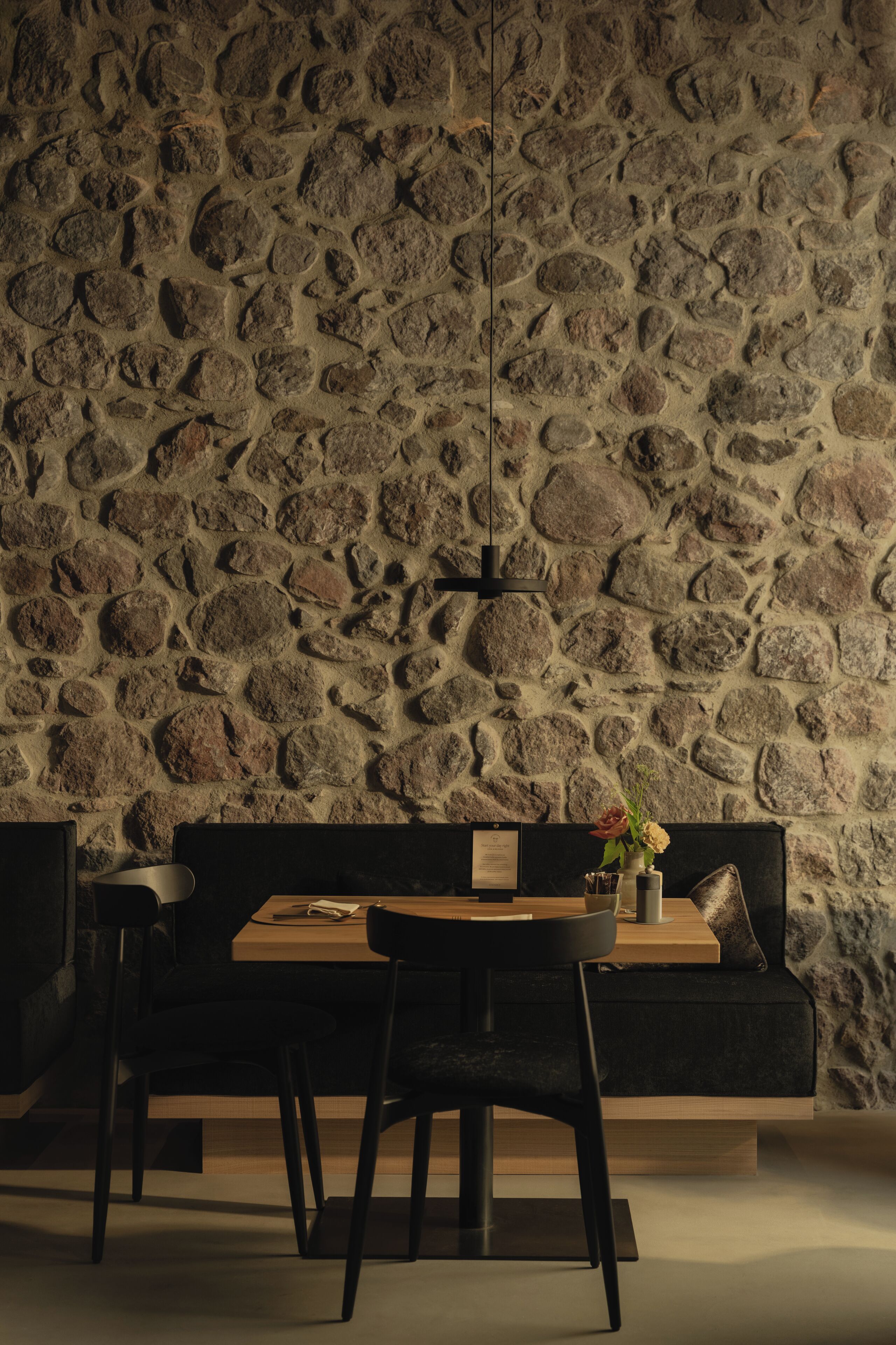 Un coin repas avec un mur en pierre, une table en bois et des chaises noires.