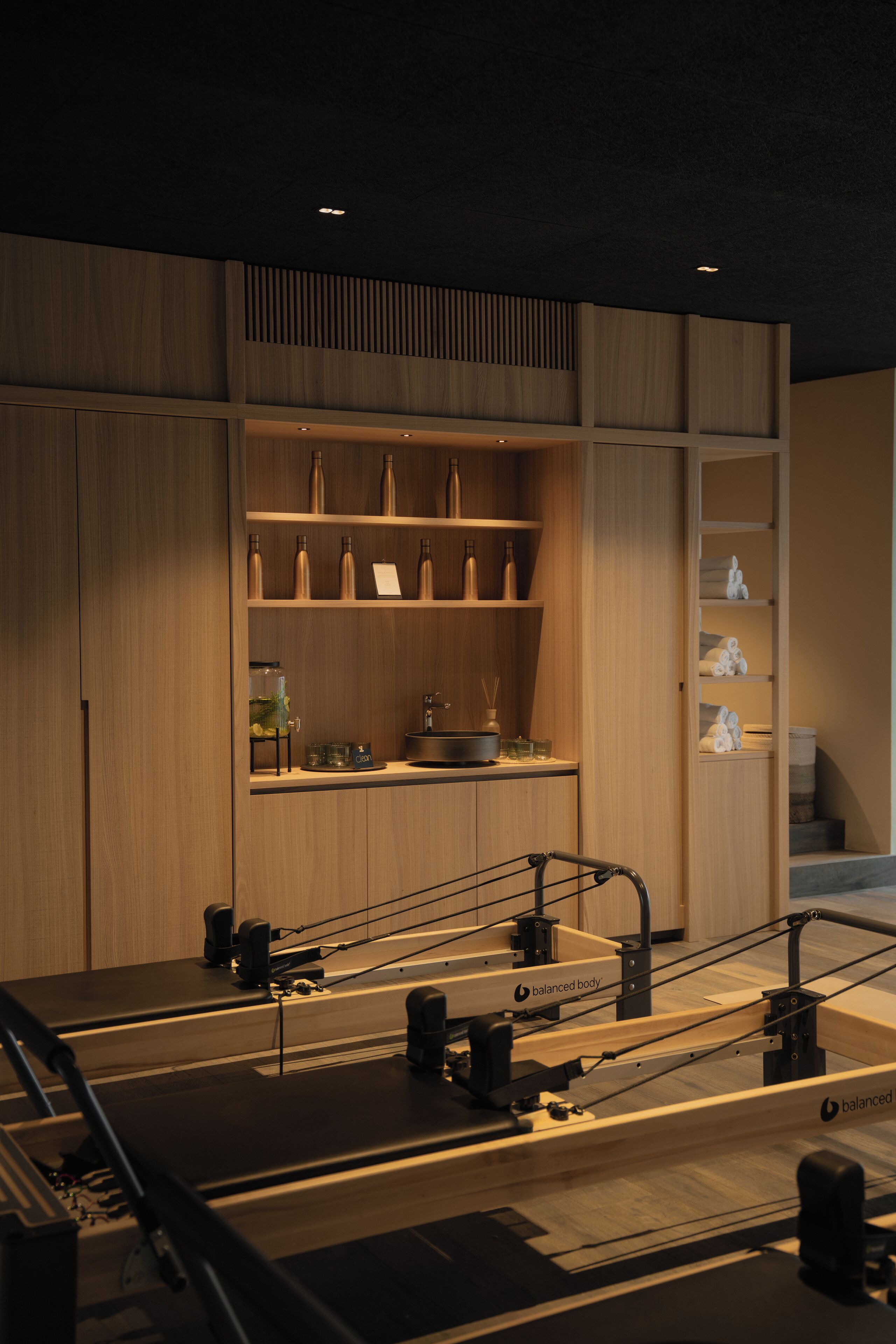 A Pilates studio with wooden walls, a mirrored wall, and a counter with bottles and towels.