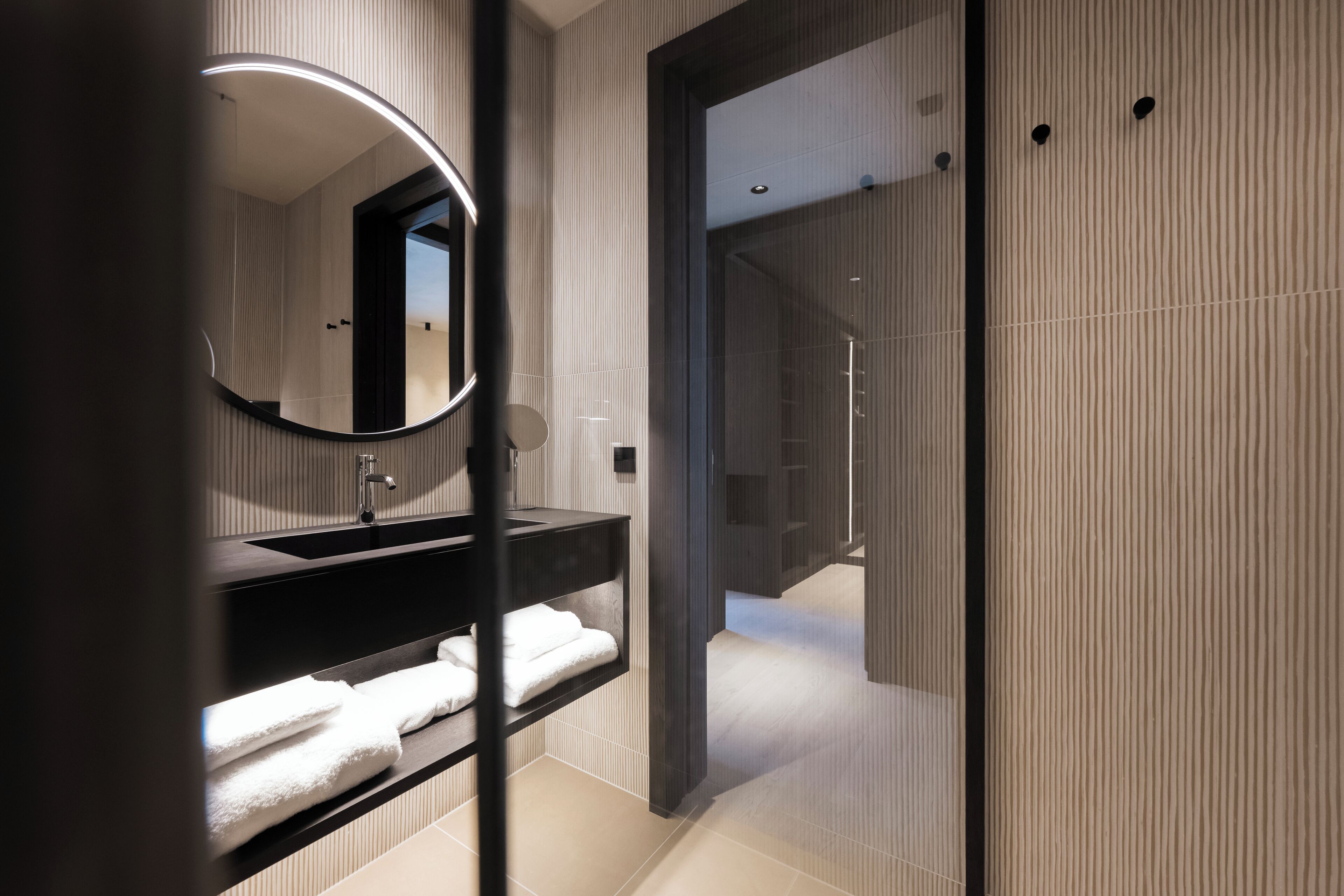 A modern bathroom with a dark vanity, a round mirror, and a glass shower enclosure.