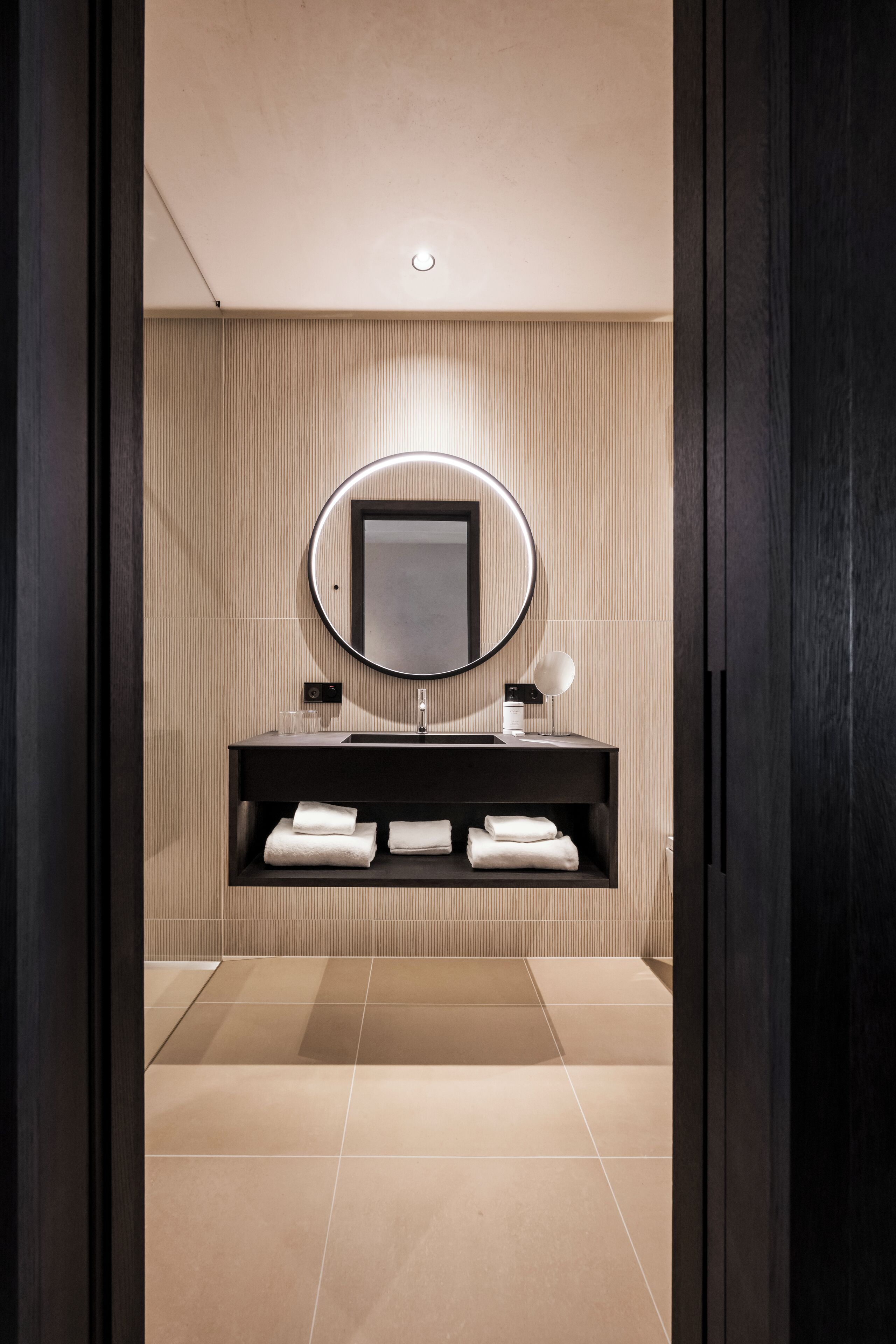 Une salle de bain moderne avec un meuble-lavabo en bois foncé, un miroir rond et un sol carrelé.