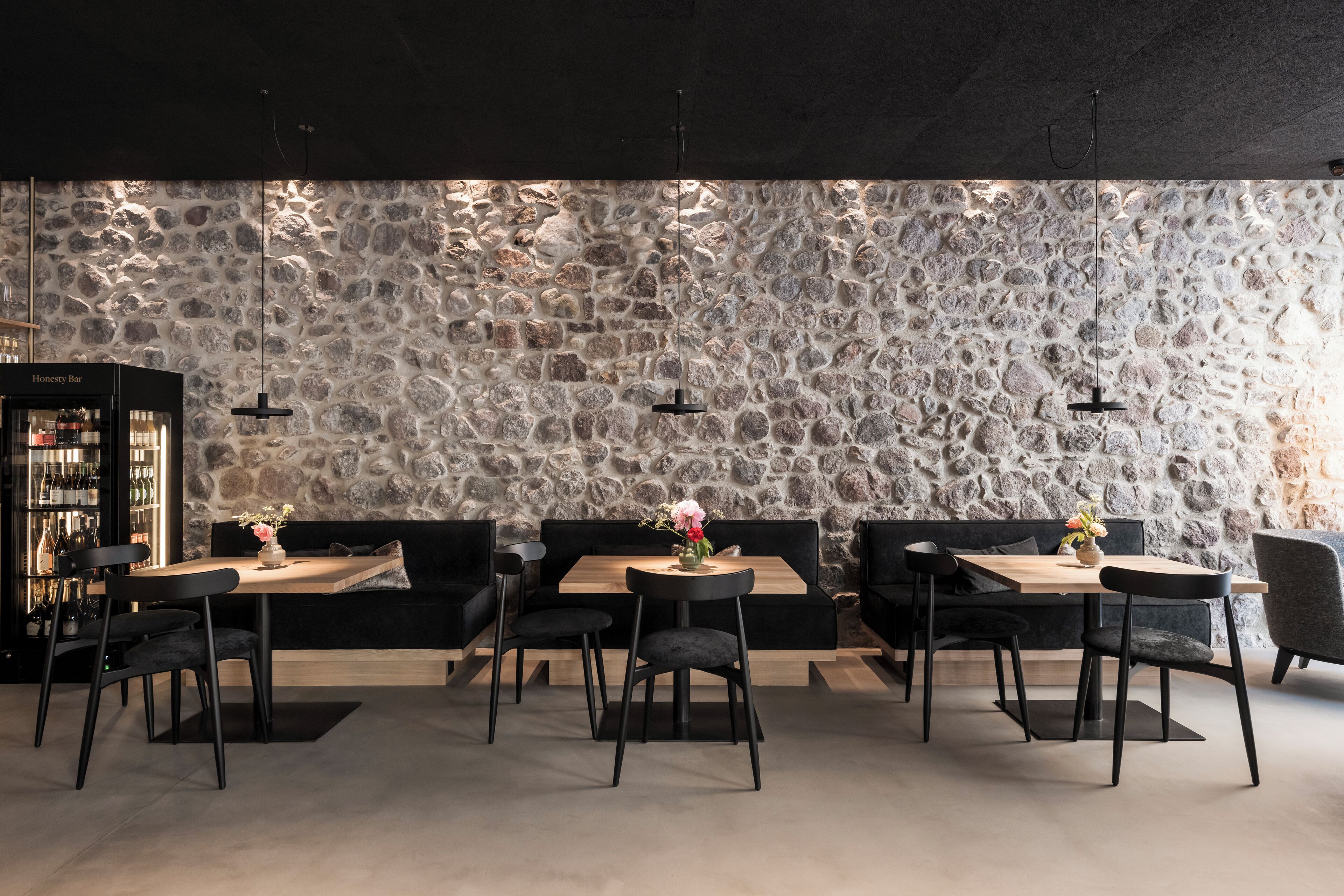 Un restaurant aux murs de pierre, doté de meubles noirs et éclairé par des suspensions.