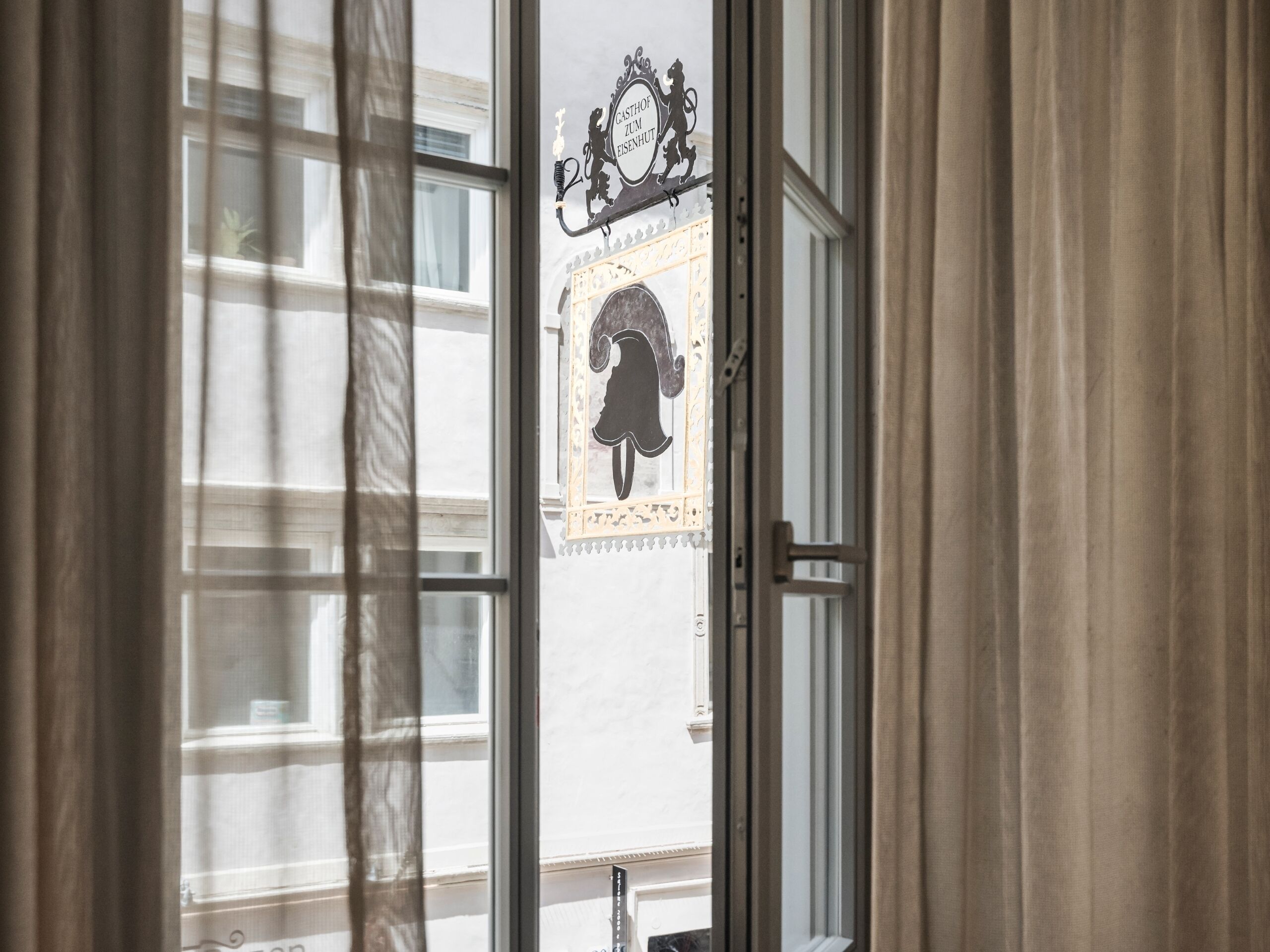 Blick durch ein Fenster auf ein dekoratives Schild mit einem Löwen und dem Schriftzug "GASTHOF ZUM EISENHURST".