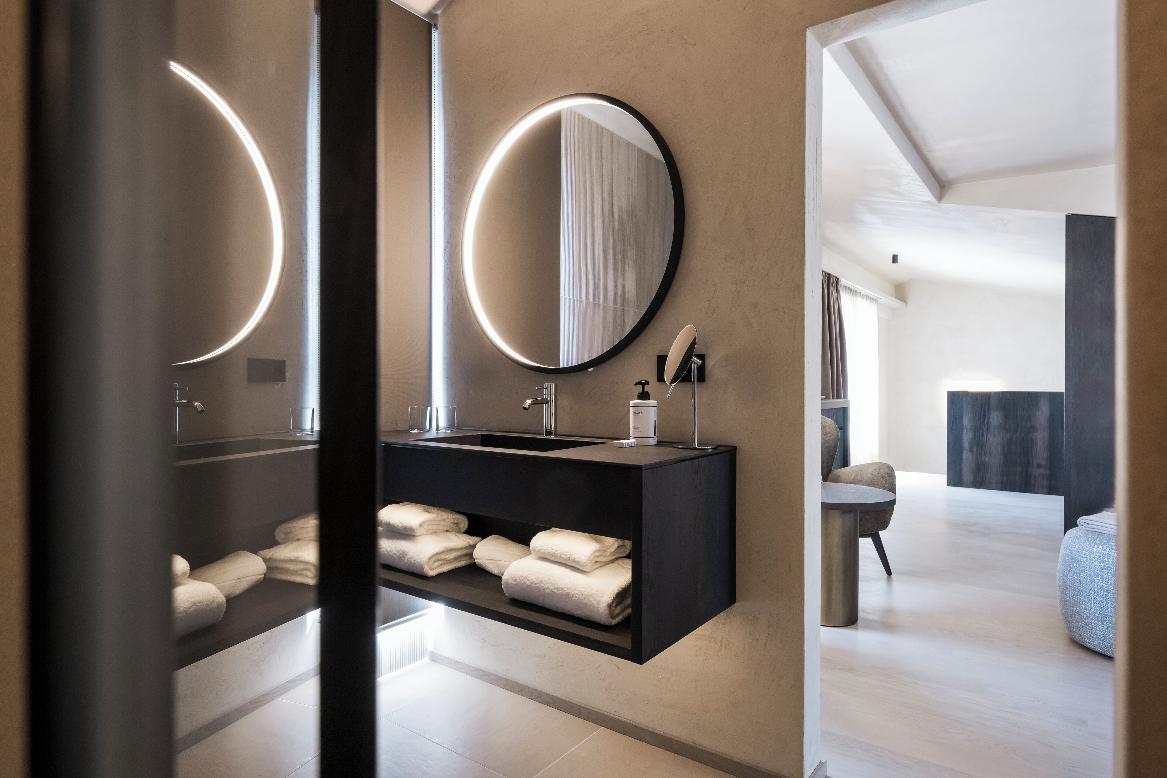 Un baño moderno con un mueble de tocador negro, dos espejos redondos y toallas dobladas con cuidado.