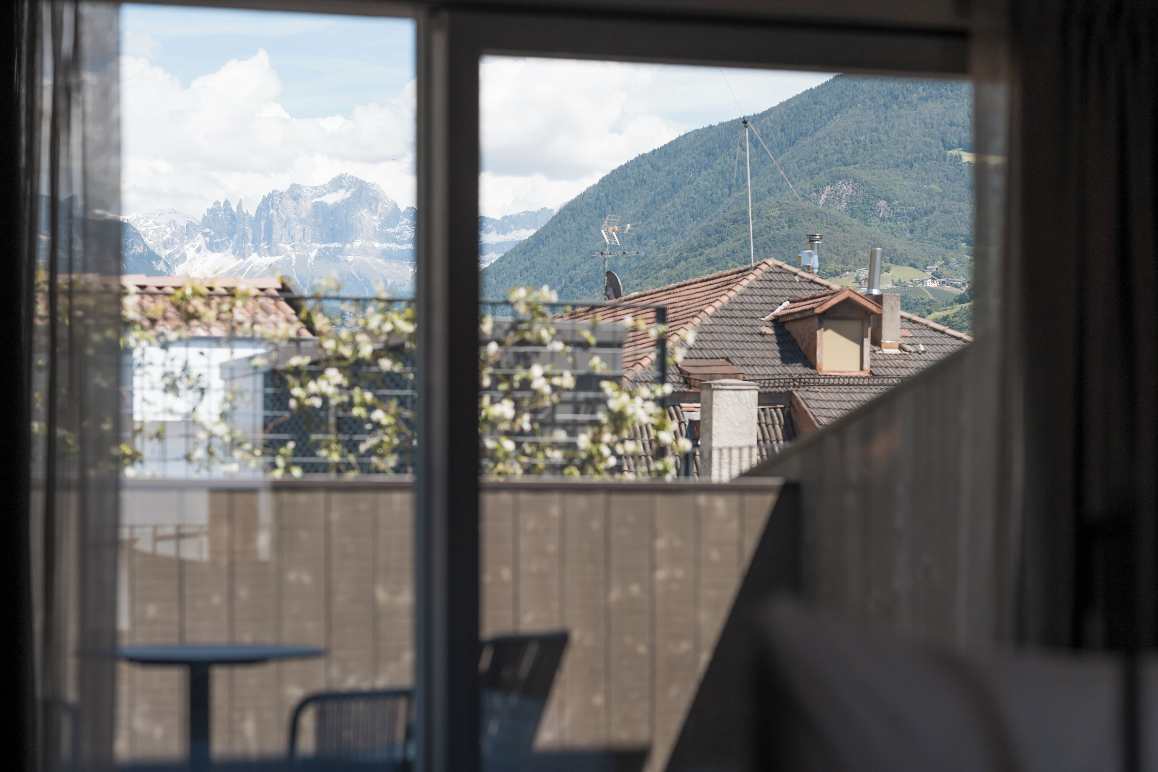 Vista desde una ventana a un paisaje montañoso con una terraza de madera y mobiliario exterior.