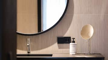 Un baño moderno con un espejo redondo, un grifo, un dispensador de jabón y un enchufe en la pared.