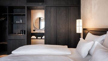 A modern hotel room with a large bed, a built-in wardrobe, a vanity with a mirror, and a bedside lamp.