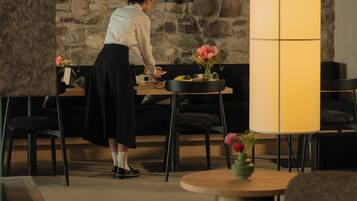 Una persona organizando objetos sobre una mesa en una habitación con pared de piedra y un panel alto, iluminado.
