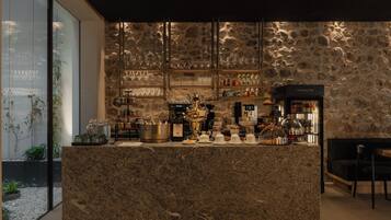 Zona de bar con pared de piedra, estantes con botellas y mostrador con diversos artículos.