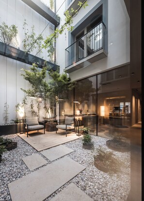 A modern outdoor seating area with a glass wall, a wooden deck, and a small garden. - Eisenhut Boutique Hotel  (Bolzano)