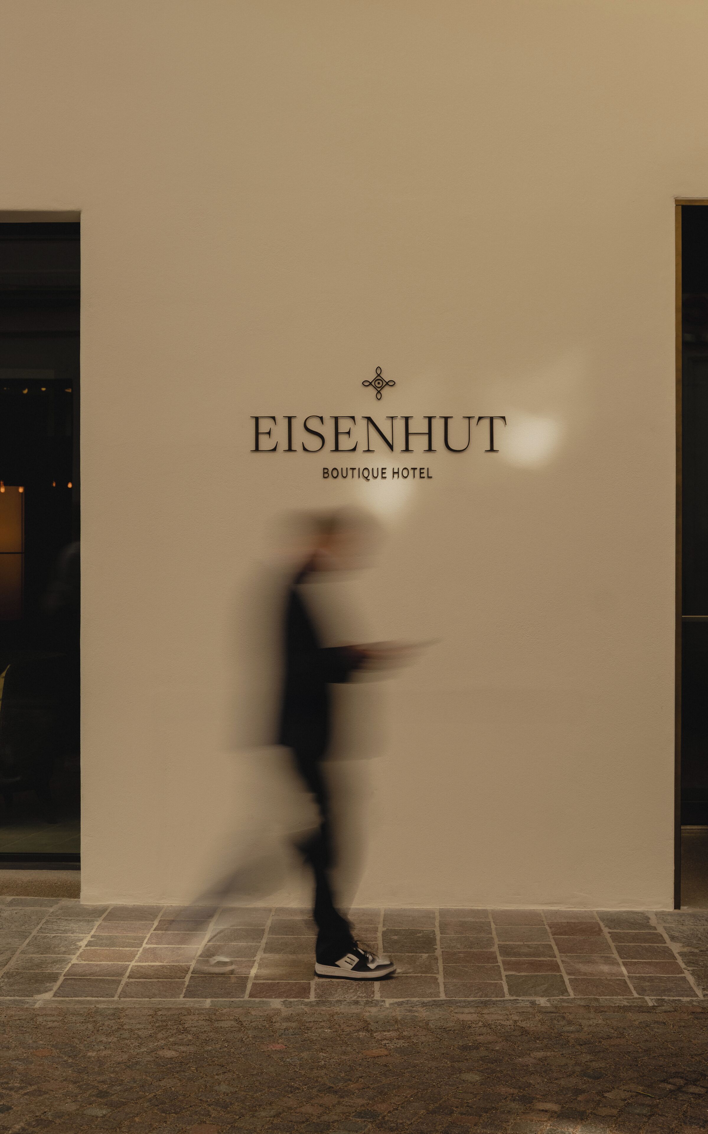 Uma pessoa passando por um edifício com uma placa que diz "EISENHUT BOUTIQUE HOTEL".