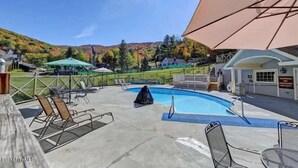 Un espace piscine comprenant des chaises longues, un coin salon abrité et un poste de surveillance pour les sauveteurs.