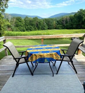 Een terras met tafel en stoelen, met uitzicht op een grasveld en bergen.