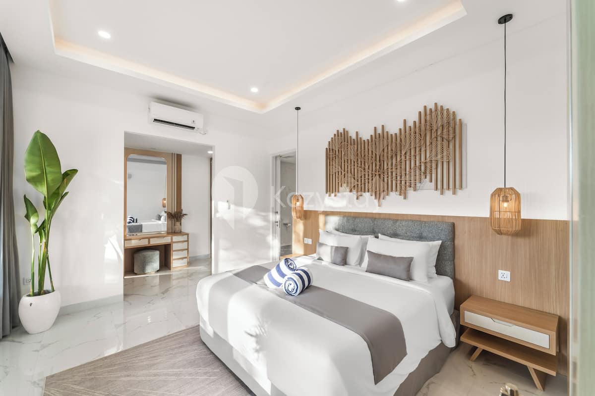 A modern bedroom with a large bed, bedside tables, a mirror, and a wall-mounted decorative piece.