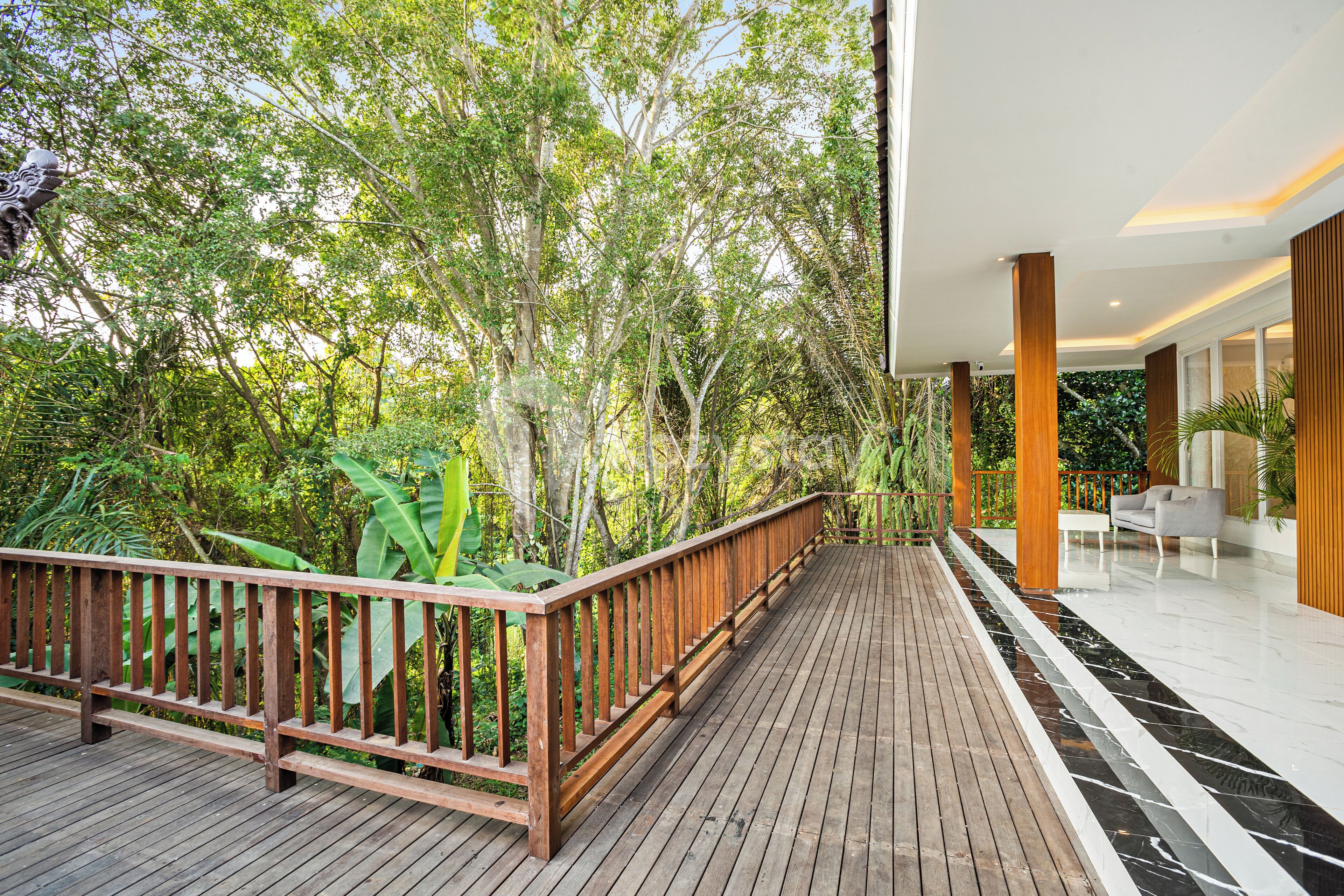 Una terraza de madera con barandilla, rodeada de vegetación exuberante y árboles.